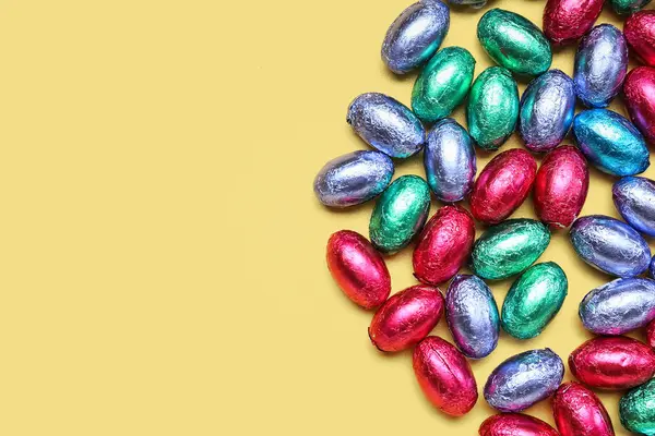 Sarı arka planda folyoda çikolatalı Paskalya yumurtaları.