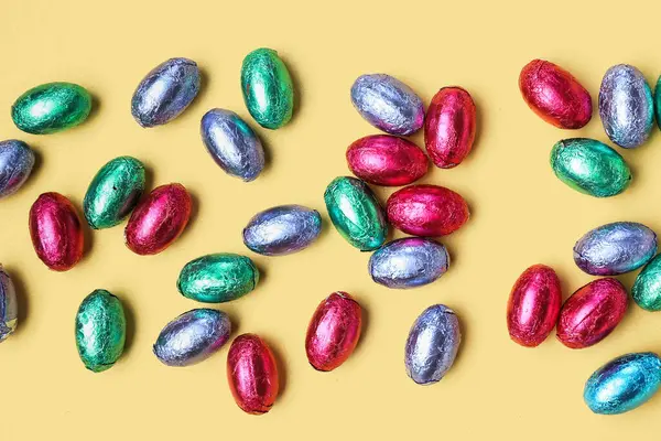 Sarı arka planda renkli folyoyla çikolatalı Paskalya yumurtaları, yakın plan.