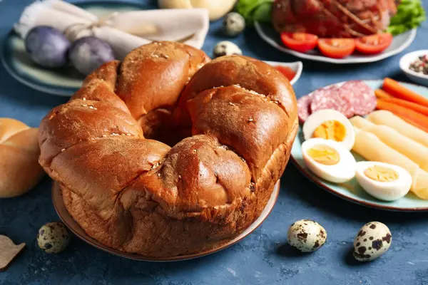 Lezzetli Paskalya çelengi ekmeği, renkli arka planda tabak ve yumurta, yakın plan.