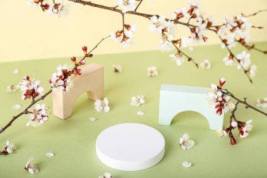 Sarı duvarın yanındaki masada çiçek açan dalları olan podyumlar. Merhaba bahar.