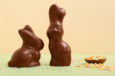 Çikolatalı Paskalya tavşanları ve renkli arka planda serpiştirilmiş yumurta.