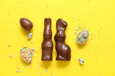 Çikolatalı Paskalya yumurtaları ve sarı arka planda tavşanlar.