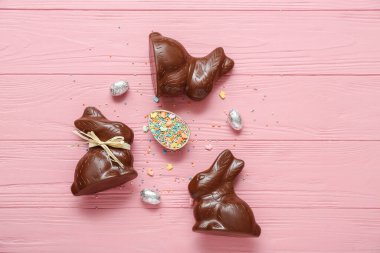 Çikolatalı Paskalya yumurtası, pembe ahşap arka planda serpiştirilmiş tavşanlar.