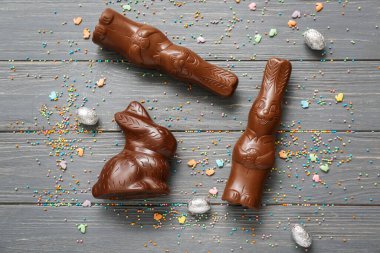 Çikolatalı tavşanlar, folyodaki Paskalya yumurtaları ve gri ahşap arka planda serpiştirmeler.