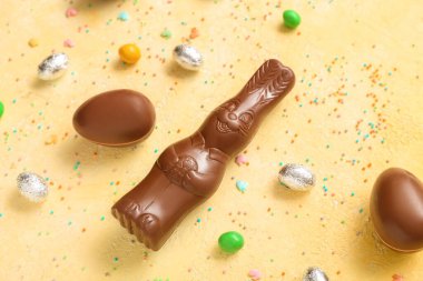 Çikolatalı Paskalya yumurtaları ve sarı arka planda küçük tavşanlar.