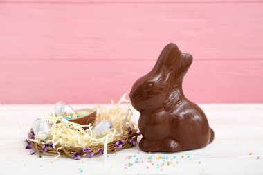 Çelenkli Paskalya tavşanı ve beyaz ahşap masaya serpiştirilmiş çikolata yumurtası.