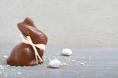Çikolata tavşanı, folyoda Paskalya yumurtası ve gri ahşap masaya serpiştirilmiş.