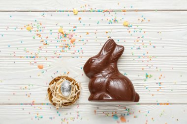 Çelenkli çikolatalı tavşan ve beyaz ahşap arka planda folyoda paskalya yumurtası.