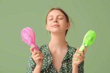 Yeşil arka planda mini vantilatörleri olan güzel genç bir kadın.