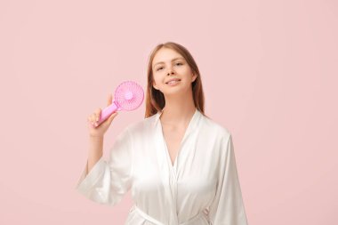 Pembe arka planda mini vantilatörü olan güzel genç bir kadın.