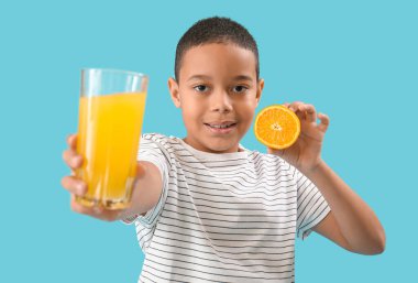Mavi arka planda bir bardak meyve suyu ve portakallı küçük Afro-Amerikalı çocuk.