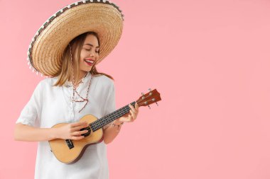 Şapkalı genç bir kadın pembe arka planda gitar çalıyor. Meksika Ölüler Günü (El Dia de Muertos) kutlamaları
