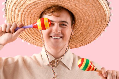Sombrero 'lu genç Meksikalı adam portresi ve pembe arka planda marakas.