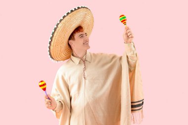 Sombrero, panço ve pembe arka planda marakas giyen Meksikalı genç bir adamın portresi.