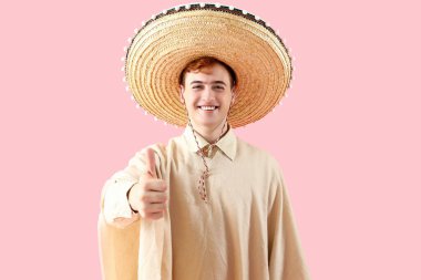 Sombrero 'lu genç Meksikalı adamın portresi pembe arka planda baş parmağını gösteriyor.