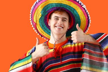 Sombrero ve pançolu mutlu Meksikalı genç adam turuncu arka planda baş parmağını kaldırıyor.