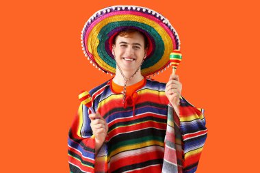 Sombrero 'lu genç Meksikalı adam portresi ve turuncu arka planda marakas.