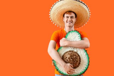 Sombrero 'lu genç Meksikalı adam portresi ve turuncu arka planda avokado şeklinde pinata.