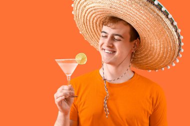Sombrero giymiş Meksikalı genç bir adamın portresi ve turuncu arka planda margarita kokteyli.
