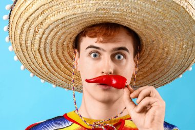 Sombrero giymiş, mavi arka planda kırmızı biberli, şaşırmış genç Meksikalı bir adamın portresi.