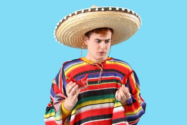 Sombrero giymiş genç Meksikalı bir adamın portresi ve mavi arka planda kırmızı biberli.