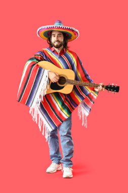 Kırmızı arka planda gitar çalan yakışıklı Meksikalı genç adam.