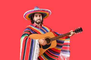 Kırmızı arka planda gitar çalan yakışıklı Meksikalı genç adam.