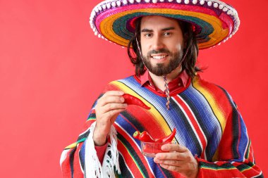 Kırmızı arka planda kırmızı biberli yakışıklı Meksikalı genç adam.