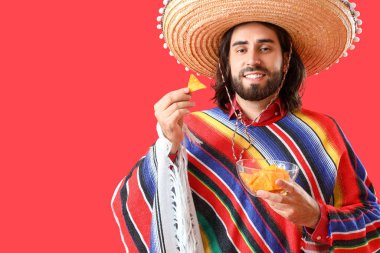 Kırmızı arka planda cips yiyen yakışıklı Meksikalı genç adam.