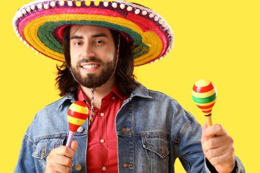Sombrero 'daki yakışıklı Meksikalı genç adam ve sarı arka planda marakas.