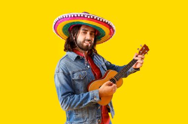Sombrero 'lu yakışıklı Meksikalı genç adam sarı arka planda gitar çalıyor.