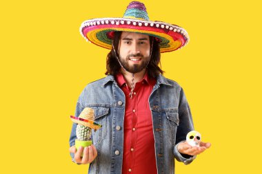 Kaktüslü yakışıklı Meksikalı genç adam ve sarı arka planda boyalı kafatası. Ölüler Günü Kutlaması