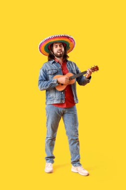 Sombrero 'lu yakışıklı Meksikalı genç adam sarı arka planda gitar çalıyor.