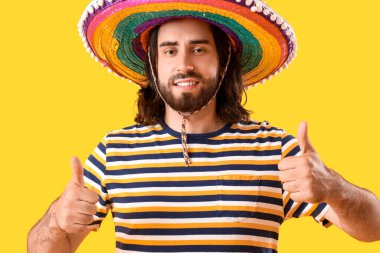Sombrero 'lu yakışıklı Meksikalı genç adam sarı arka planda baş parmağını kaldırıyor.