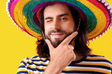 Sarı arka planda sombrero giyen yakışıklı Meksikalı genç adam.