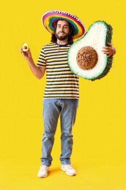 Avokado ve sarı arka planda pinyatası olan, Sombrero 'lu yakışıklı Meksikalı genç adam.