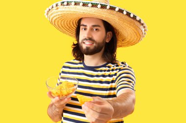 Sombrero 'lu yakışıklı Meksikalı genç adam ve sarı arka planda nachos.