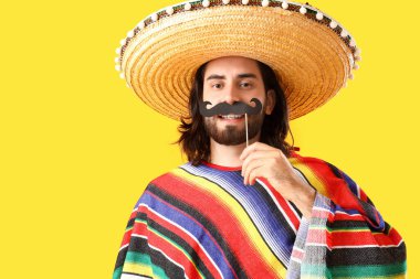 Sombrero giymiş, sarı arka planda kağıt bıyıklı genç bir Meksikalı.