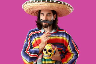 Mor arka planda boyalı kafatası ve kağıt bıyıklı yakışıklı bir Meksikalı. Ölüler Günü Kutlaması