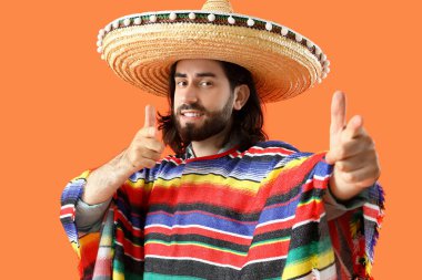 Sombrero giyen havalı genç Meksikalı adam ve turuncu arka planda panço