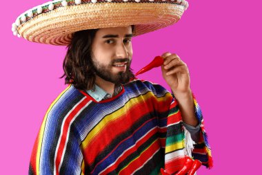 Sombrero 'daki yakışıklı Meksikalı genç adam ve mor arka planda kırmızı biberli.