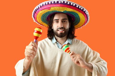 Sombrero ve pançolu yakışıklı genç adam turuncu arka planda marakas çalıyor.
