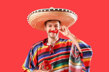 Kırmızı arka planda kırmızı biberli genç Meksikalı adam.