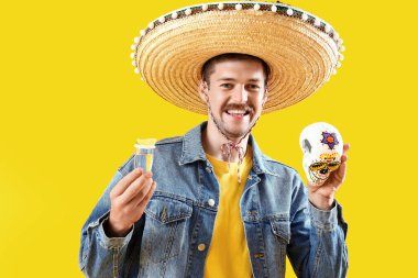 Sarı arka planda boyalı kafatası ve tekilayla yakışıklı bir Meksikalı. Ölüler Günü Kutlaması