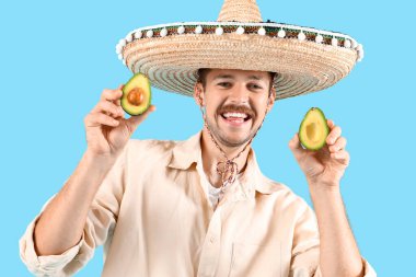 Sombrero 'lu genç Meksikalı adam ve mavi arka planda avokadosu var.