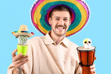 Mavi arka planda davul, kaktüs ve kafatası olan genç Meksikalı adam.