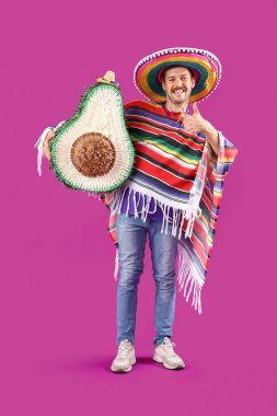 Avokado pinyatası olan genç Meksikalı adam morarmış arka planda baş parmak gösteriyor.