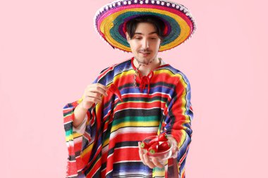 Pembe arka planda kırmızı biberli genç Meksikalı adam.