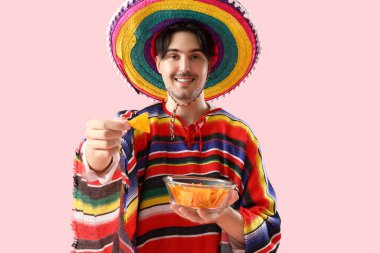 Pembe arka planda cipsleri olan genç Meksikalı adam.