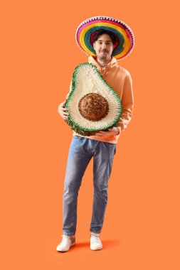 Turuncu arka planda avokado pinyatası olan genç Meksikalı adam.